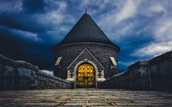 A 4K Ultra HD nighttime view of a man-made stone castle tower with an illuminated wooden door under a dramatic cloudy sky.