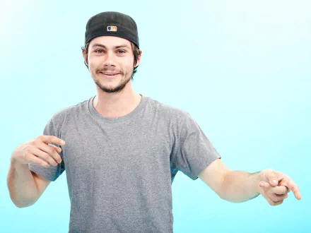 HD desktop wallpaper featuring a cheerful man in a gray t-shirt and a baseball cap against a light blue background.