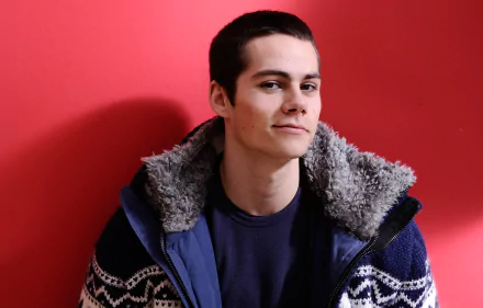 HD desktop wallpaper featuring a person with a subtle smile, wearing a jacket with fur lining, against a red background.
