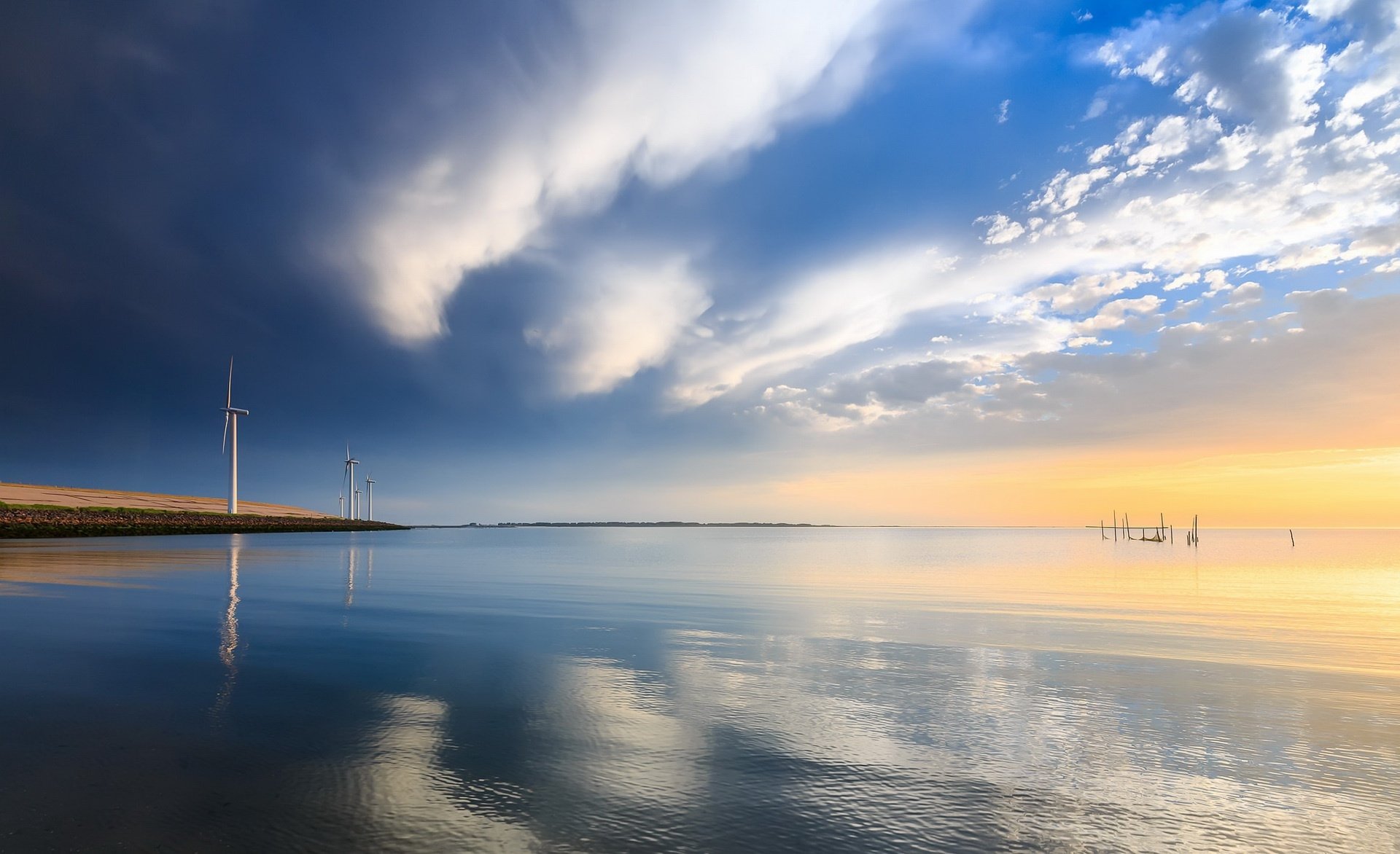 HD PC desktop wallpaper: coastal wind turbines under a dramatic sky and clouds, sunlit horizon reflected on calm ocean water.