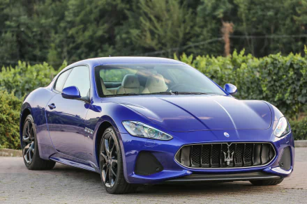 HD desktop wallpaper featuring a blue Maserati GranTurismo coupe, a luxurious supercar and grand tourer, parked outdoors against a green leafy backdrop.