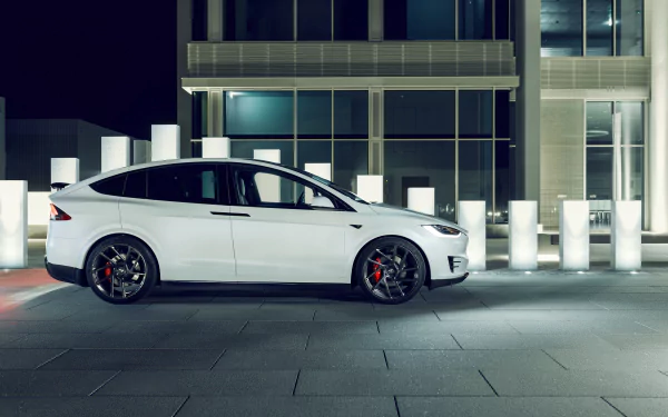 White Tesla Model X parked before a modern building at night — Tesla Motors vehicle showcased as a 4K Ultra HD PC desktop wallpaper/background.