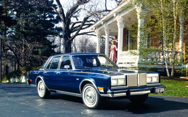 HD PC desktop wallpaper of a blue Chrysler LeBaron car parked on a driveway in front of a Victorian house, vehicle centered as a Chrysler sedan background.