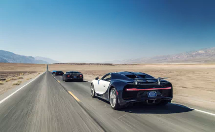 HD desktop wallpaper featuring multiple Bugatti Chiron supercars driving on a long, straight road through a vast desert landscape under a clear blue sky.