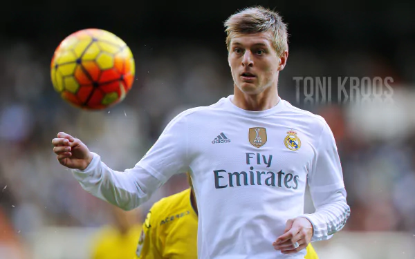 Toni Kroos in Real Madrid C.F. white jersey focused on a soccer ball during a match, captured in a 4K Ultra HD sports wallpaper.