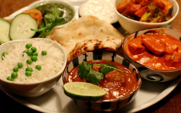 A vibrant HD PC desktop wallpaper featuring a delicious spread of Indian food, including rice with peas, naan bread, curry dishes, and fresh vegetables.