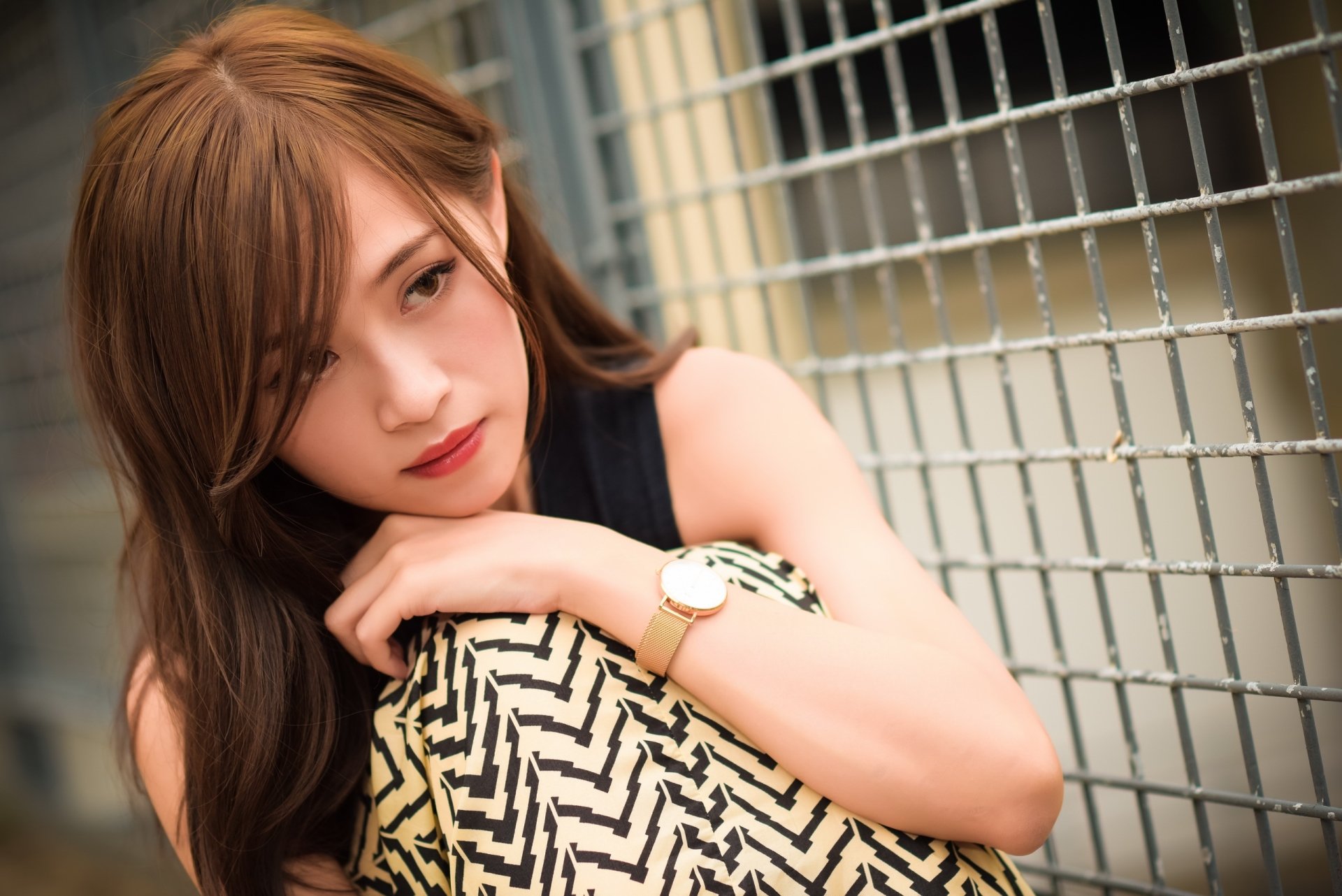 HD desktop wallpaper featuring an Asian brunette model with brown eyes, leaning against a wire fence and holding a patterned pillow.