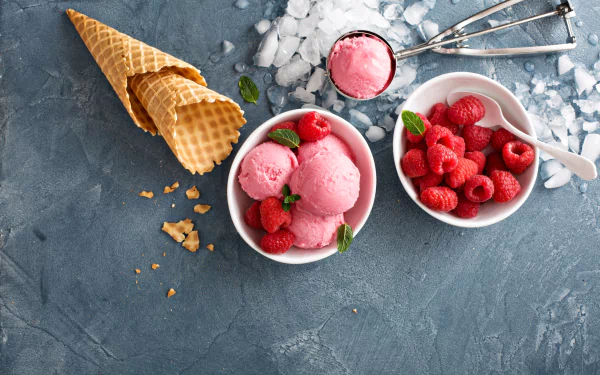 4K Ultra HD still life of raspberry ice cream scoops in a bowl, fresh raspberries in another bowl, waffle cones, and ice cream scoops on a textured blue surface.