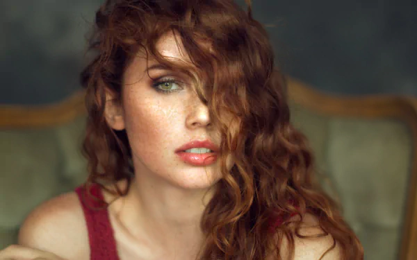 Close-up portrait of a redheaded woman model with green eyes and freckles, tousled hair partially covering her face — HD PC desktop wallpaper and background.