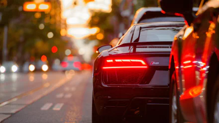 HD desktop wallpaper featuring the rear view of a sleek Audi R8 vehicle illuminated by vibrant city lights at dusk.
