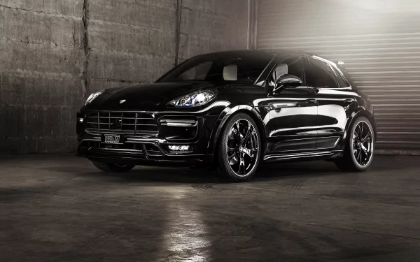 Black Porsche Macan SUV in a dim concrete garage with glossy finish and sporty wheels — 2K Quad HD PC desktop wallpaper background.