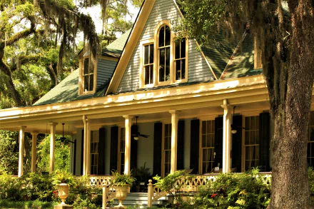 4K Ultra HD PC desktop wallpaper and background: sunlit mansion house with wide wraparound porch framed by Spanish-moss-draped trees, man-made architectural details and lush foreground plants.