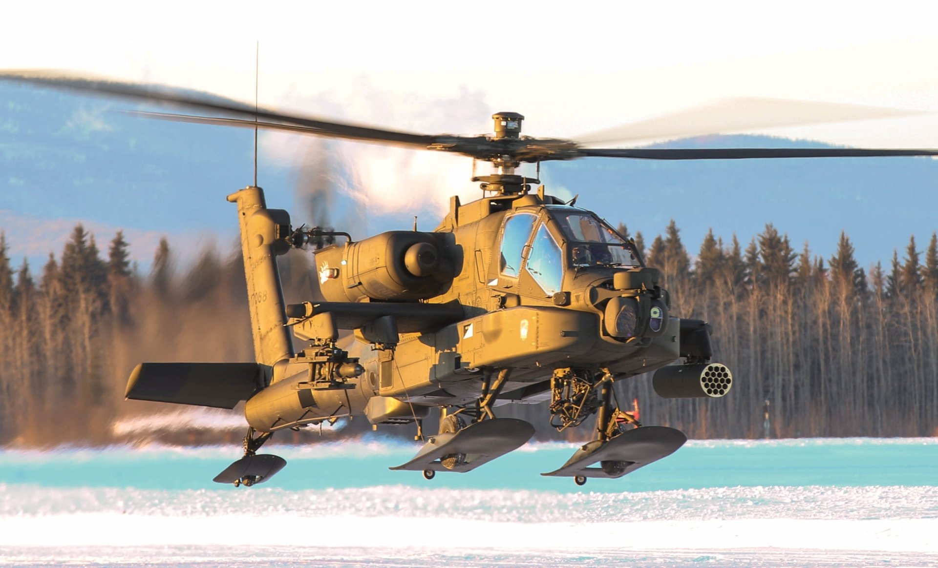 HD desktop wallpaper showcasing a Boeing AH-64 Apache military helicopter flying low over a snowy landscape with a forest backdrop.