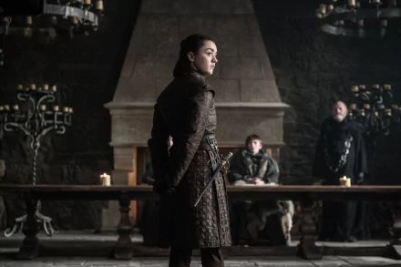 Arya Stark, portrayed by Maisie Williams, stands in a dimly lit room with Bran Stark (Isaac Hempstead-Wright) and a third character from Game of Thrones.