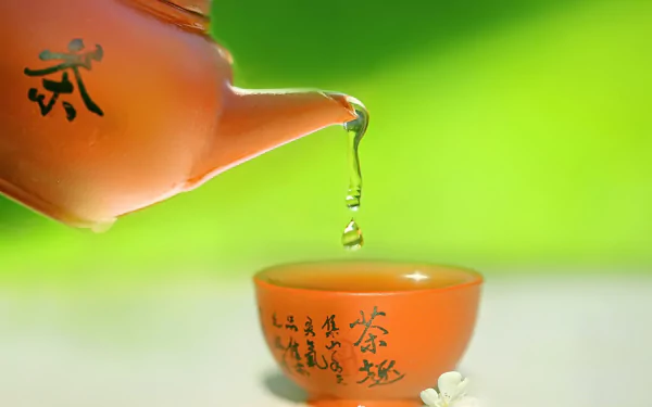 HD desktop wallpaper featuring an oriental tea cup with tea pouring from a matching teapot, set against a vibrant green background.