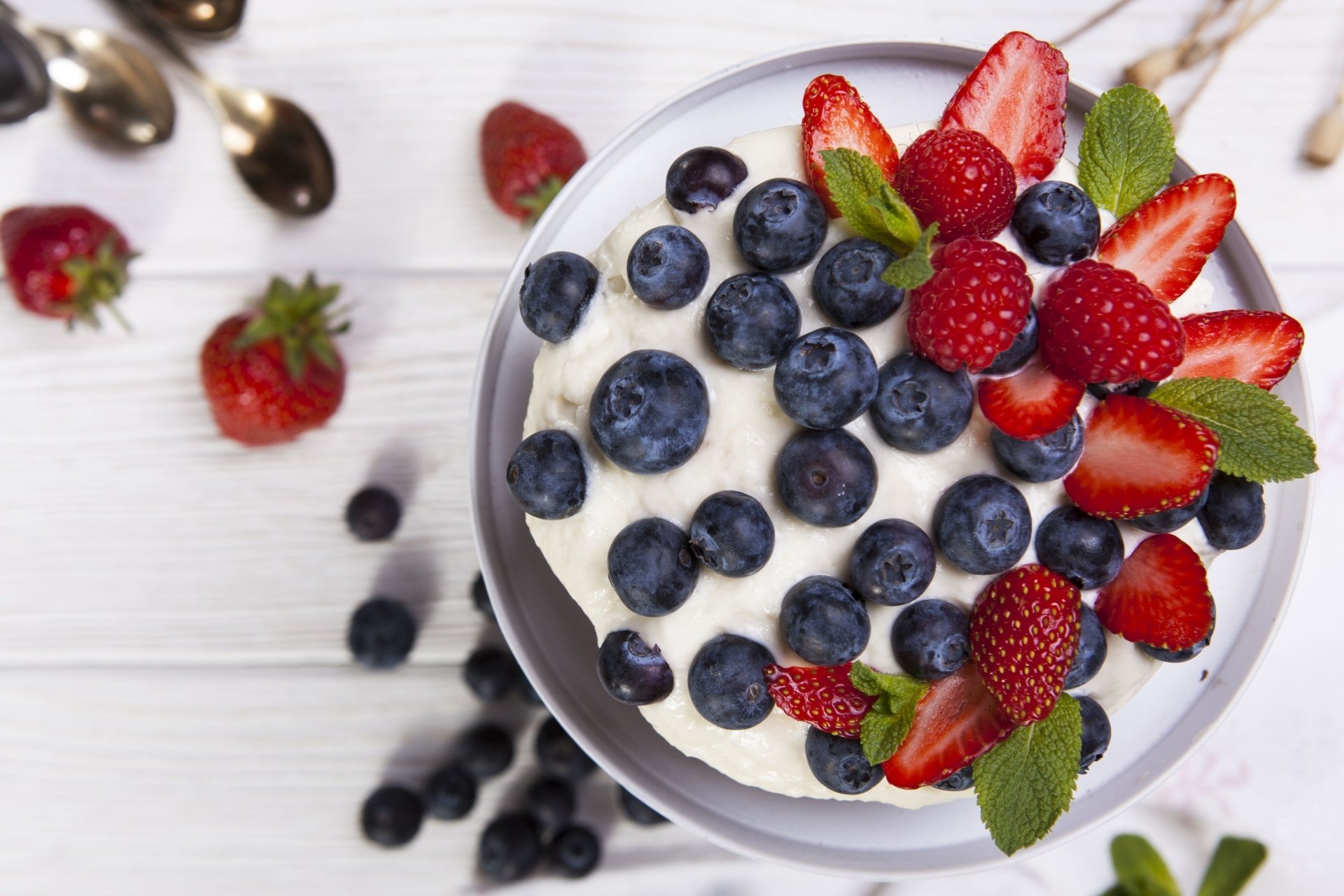 HD desktop wallpaper featuring a bowl of ice cream topped with fresh strawberries, raspberries, blueberries, and mint leaves on a white wooden surface.