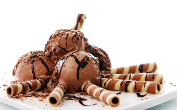 Close-up of chocolate ice cream scoops drizzled with chocolate sauce and surrounded by striped wafer rolls on a white plate, captured in stunning 4K Ultra HD.