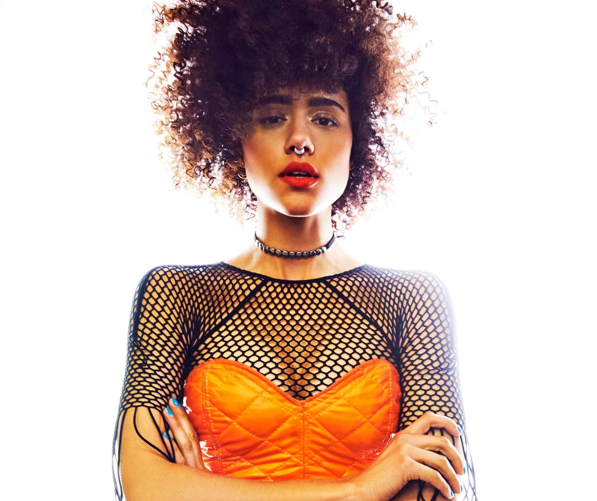 HD PC wallpaper of a brunette woman with curly hair, brown eyes and bold lipstick, wearing a choker and nose piercing, orange corset over a black fishnet top.