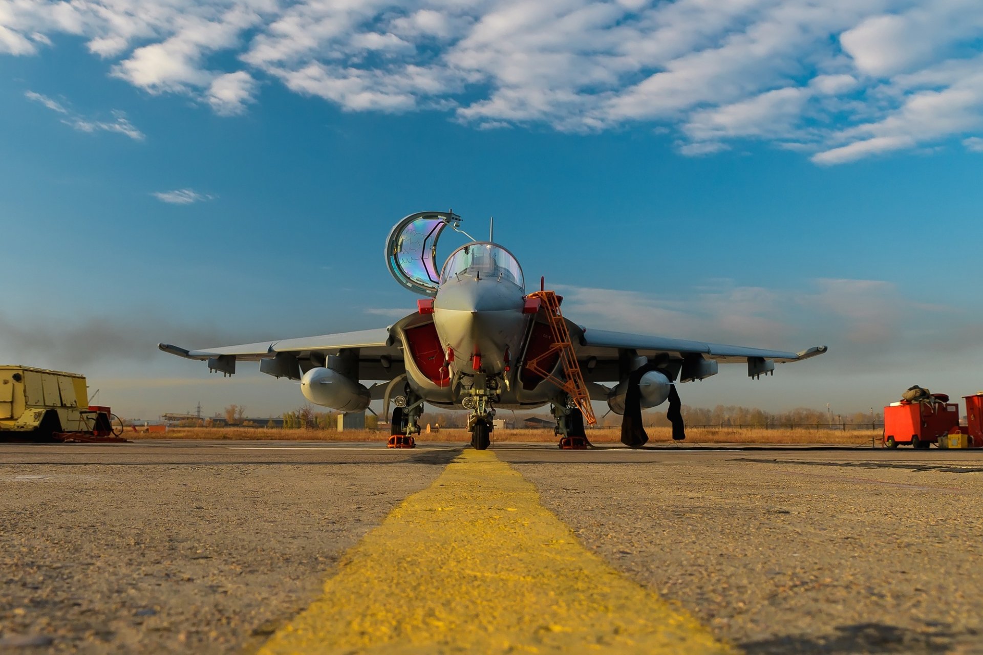 Front view of a Yakovlev Yak-130 military jet fighter warplane on a runway under a partly cloudy sky, captured in high-definition for a desktop wallpaper.