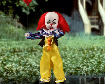 HD desktop wallpaper featuring a figurine of Pennywise from the 1990 movie It standing in a grassy field, with a creepy, colorful clown costume and red hair.
