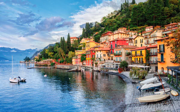 Colorful houses line the waterfront village of Lake Como, Italy, nestled against lush green hills under a partly cloudy sky in this 4K Ultra HD desktop wallpaper.