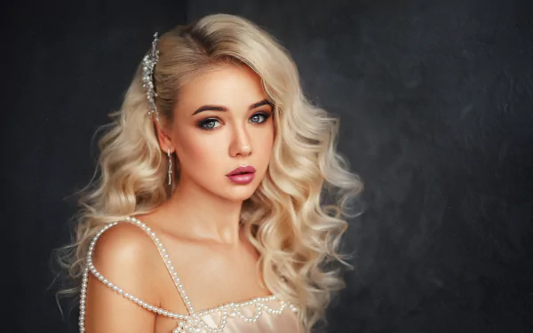 A blonde model with blue eyes and curled hair, adorned with a hair accessory and wearing lipstick, poses in a high-definition wallpaper background.