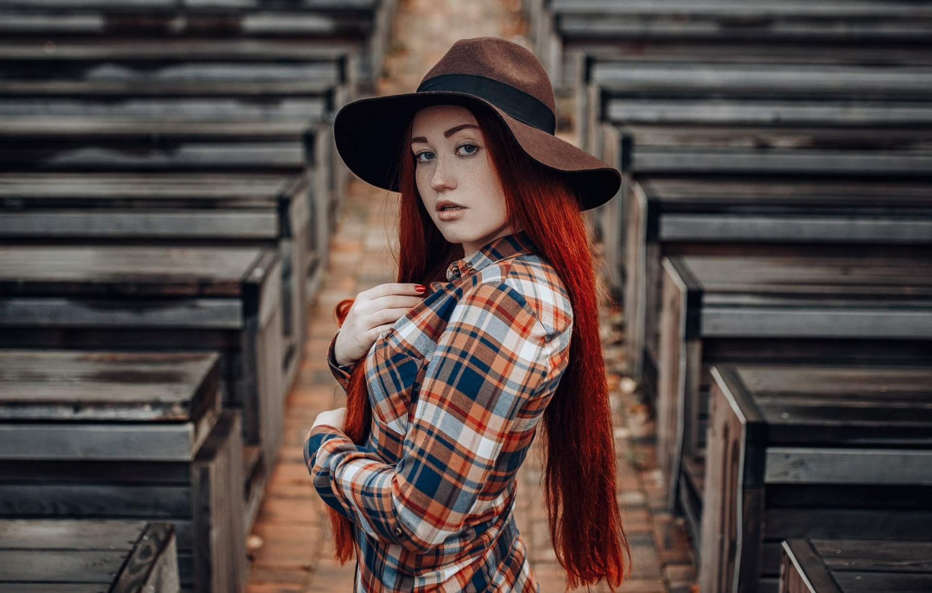 2K Quad HD PC desktop wallpaper: depth-of-field portrait of a redhead woman model with long hair, freckles and blue eyes wearing a brown hat and plaid shirt.