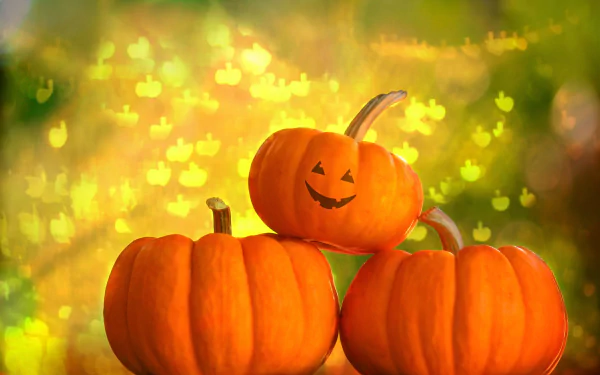 A 4K Ultra HD Halloween-themed desktop wallpaper showing three bright orange pumpkins, one carved with a smiling face, glowing against a soft, warm bokeh background.