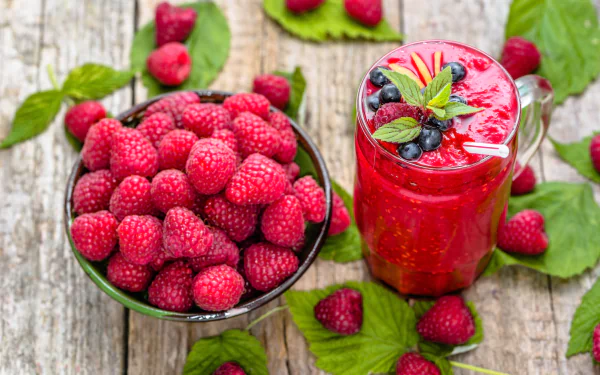 8K Ultra HD PC desktop wallpaper: still life of a raspberry smoothie in a glass with mint and berries beside a bowl of fresh raspberries on rustic wood, vibrant fruit drink photo.