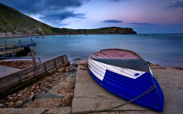 HD desktop wallpaper of a colorful boat resting on a concrete shore beside a rocky beach, with ocean waves, clouds, and a serene coastline under a vivid sky.