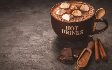 HD desktop wallpaper featuring a mug labeled HOT DRINKS filled with hot chocolate topped with marshmallows, accompanied by chocolate pieces, cinnamon sticks, and a wooden scoop with powdered chocolate.