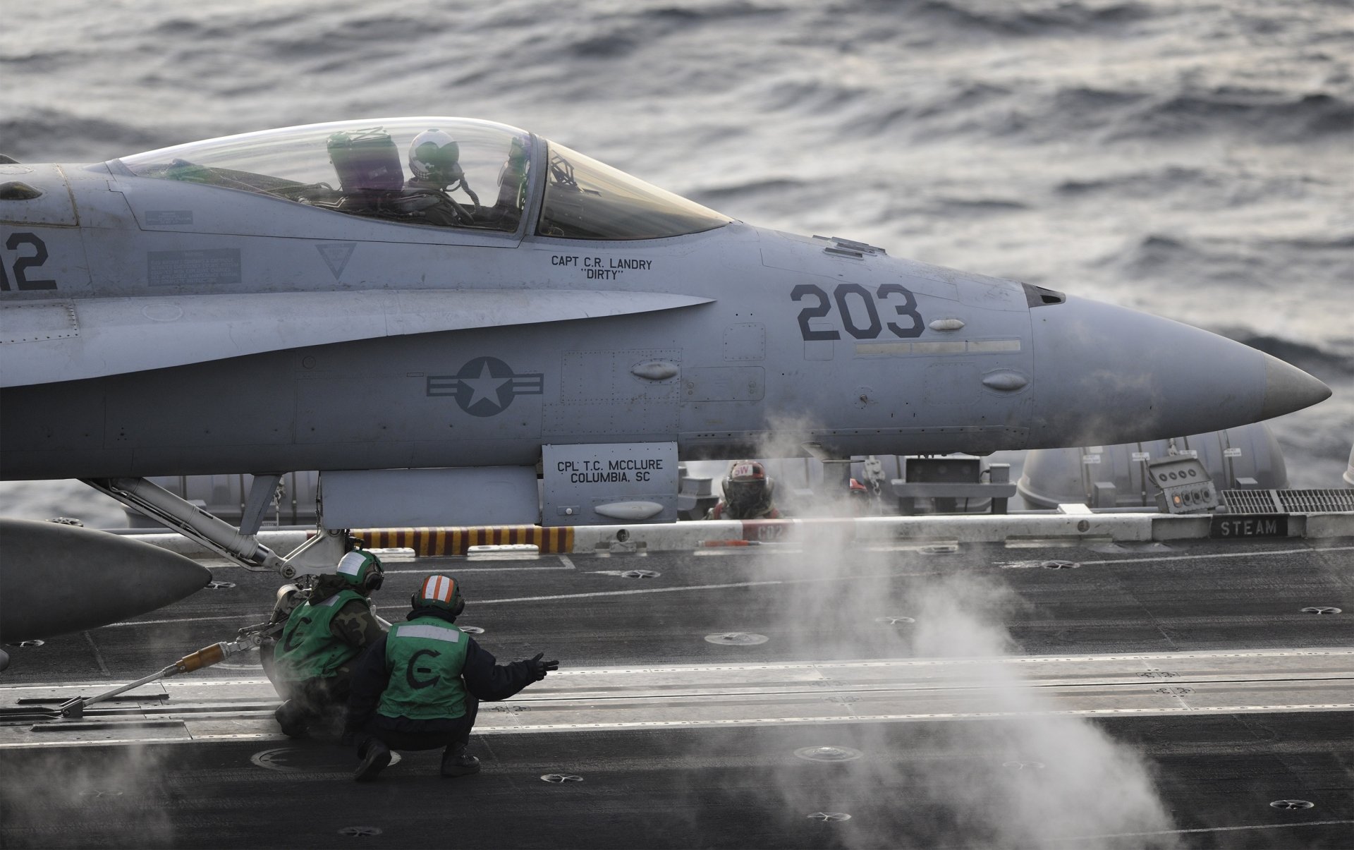 HD desktop wallpaper of a McDonnell Douglas F/A-18 Hornet jet fighter warplane on an aircraft carrier deck during military operations.