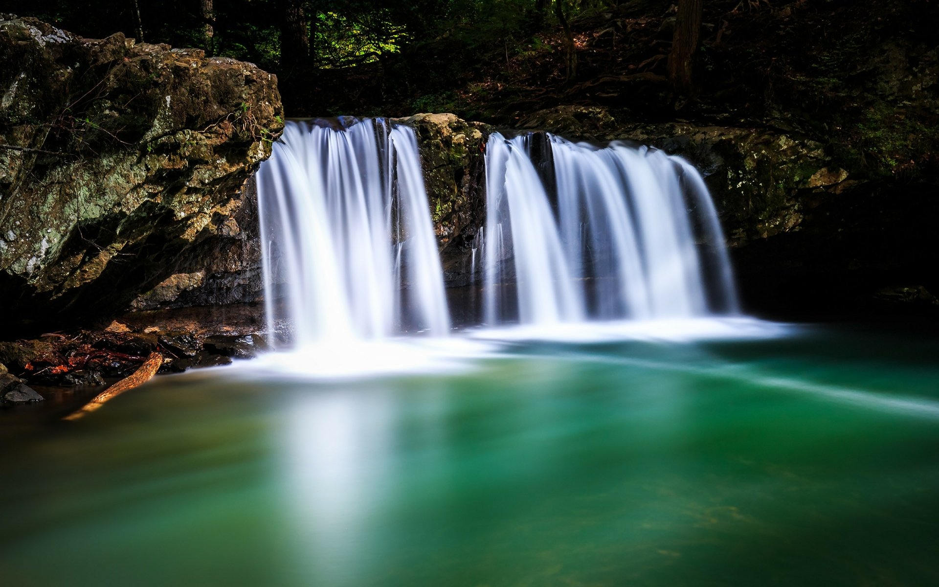 HD desktop wallpaper showcasing a serene waterfall flowing over rocks, surrounded by lush nature and foam forming on the vibrant green water below.
