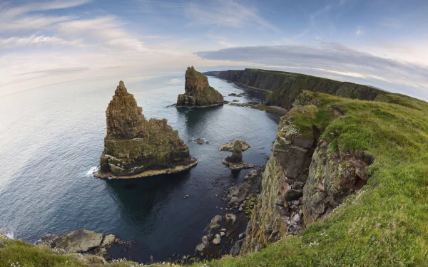 Fisheye view of towering cliffs and rocky sea stacks along Scotland’s rugged coastline under a vast sky, showcasing the natural beauty of ocean and coastal landscapes.