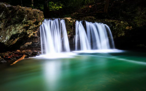 HD desktop wallpaper showcasing a serene waterfall flowing over rocks, surrounded by lush nature and foam forming on the vibrant green water below.