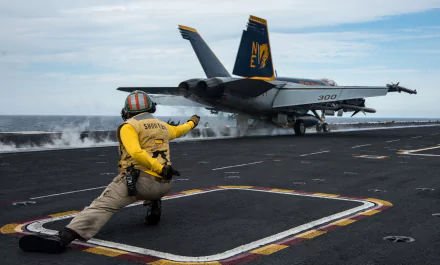 A McDonnell Douglas F/A-18 Hornet warplane taking off from an aircraft carrier, with a deck crew member guiding the jet fighter. Military HD desktop wallpaper.