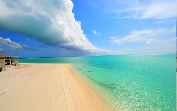 A stunning HD desktop wallpaper featuring a tropical beach with golden sand, turquoise sea, and a vast horizon capped with fluffy clouds.