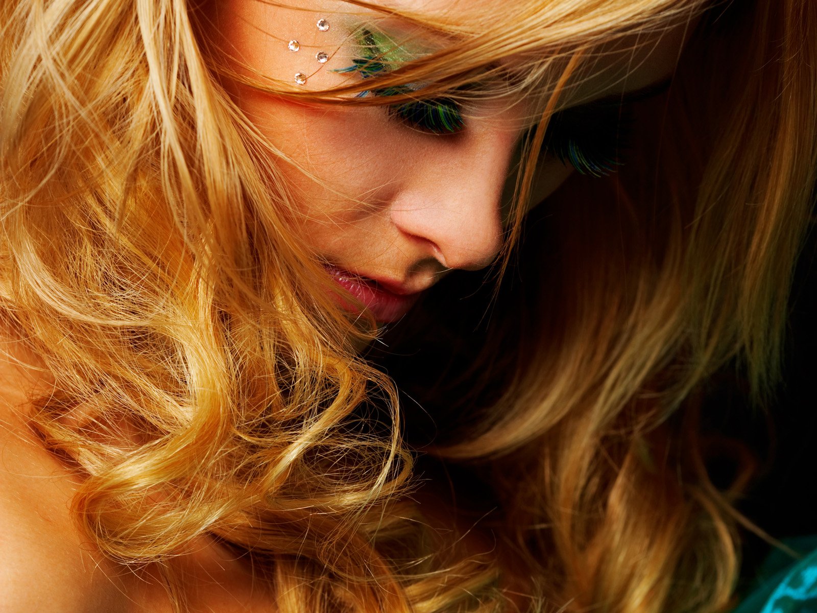 A sensual woman with flowing blonde hair gazes downward, highlighting her soft features. This stunning image serves as an HD desktop wallpaper and background.