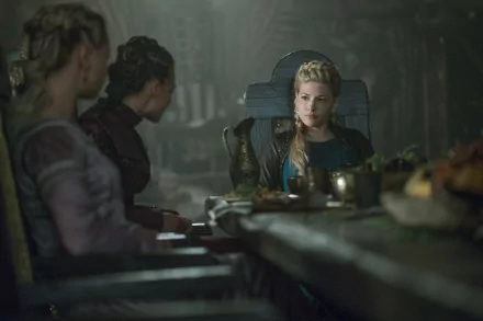 8K desktop wallpaper: blonde shieldmaiden with braided hair sits at a dim longhouse table, tense expression amid candles and wooden feastware.