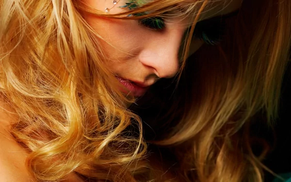 A sensual woman with flowing blonde hair gazes downward, highlighting her soft features. This stunning image serves as an HD desktop wallpaper and background.