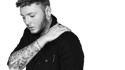 HD wallpaper featuring a monochrome portrait of a man with a visible sleeve tattoo, posing thoughtfully.