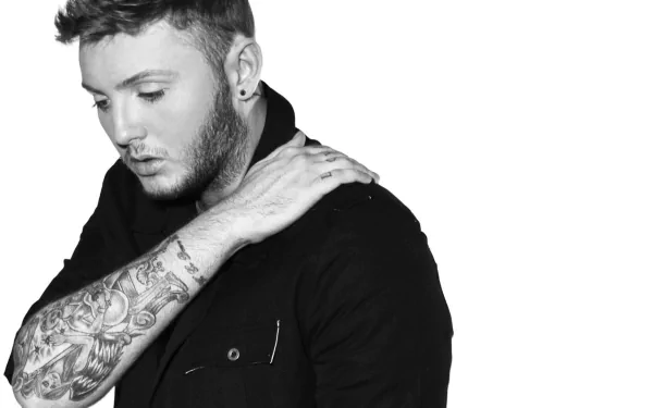 HD wallpaper featuring a monochrome portrait of a man with a visible sleeve tattoo, posing thoughtfully.