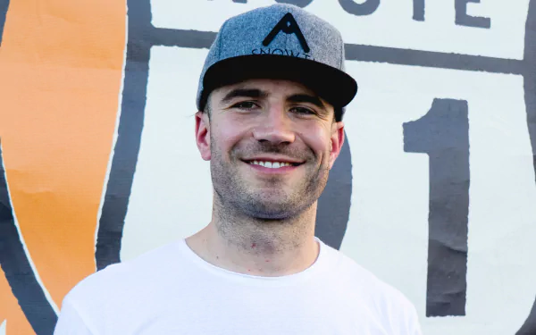 HD desktop wallpaper featuring a smiling man wearing a cap, set against a backdrop with graphic elements.