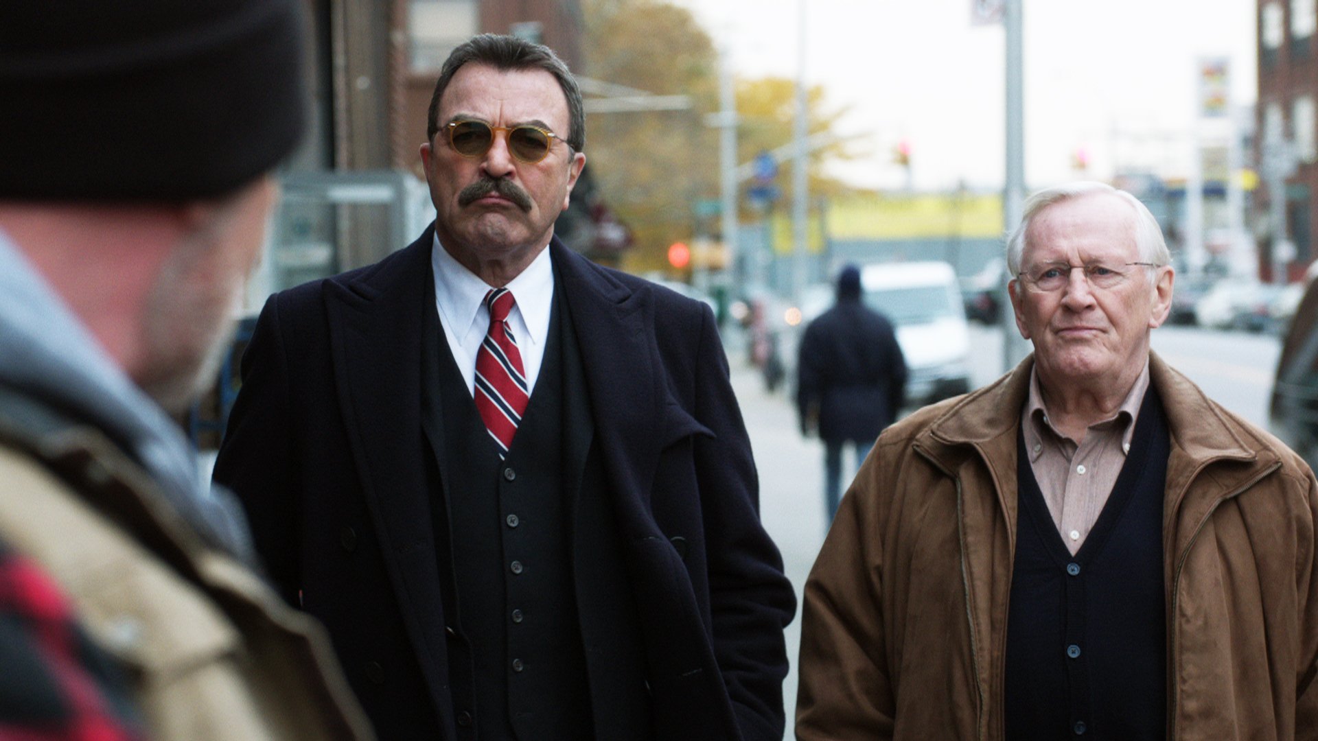 HD desktop wallpaper featuring two men from the TV series Blue Bloods, one in a suit and the other in a brown jacket, on a city street.