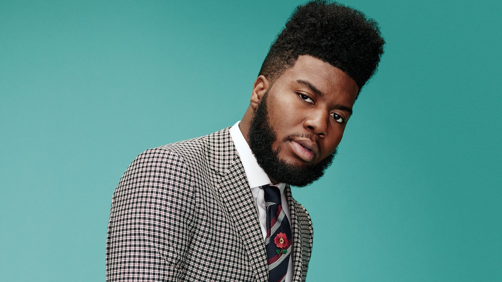 HD desktop wallpaper featuring a person with a stylish haircut, wearing a checkered suit, against a teal background. Tagged: Khalid.