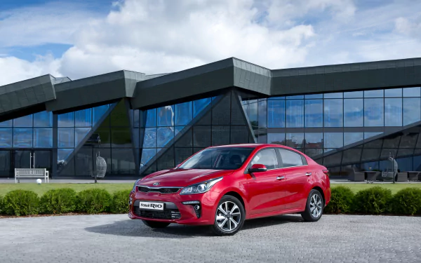 A red Kia Rio compact car parked in front of a modern glass building, captured in a sharp 4K Ultra HD desktop wallpaper.