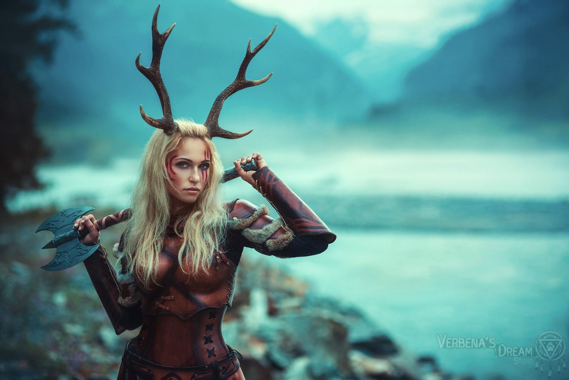 HD PC desktop wallpaper featuring a woman in detailed cosplay with antler headpiece and armor, set against a misty, blurred natural landscape background.