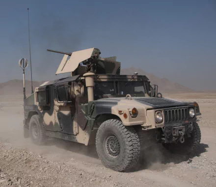A military Humvee equipped with a mounted machine gun drives through a desert landscape with a soldier manning the weapon, captured in HD for a PC desktop wallpaper.