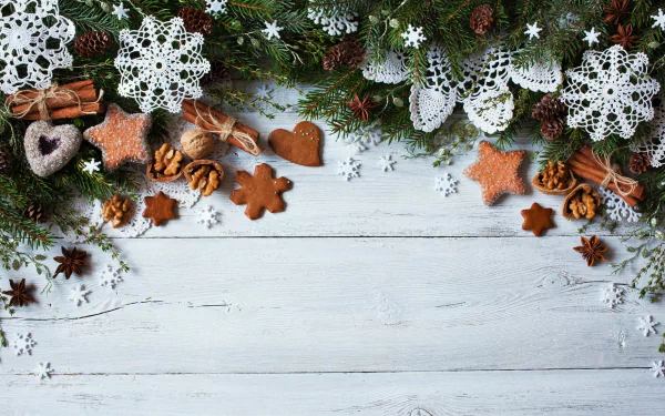 Holiday-themed HD desktop wallpaper featuring cinnamon sticks, pine cones, crocheted snowflake decorations, and festive cookies arranged on a rustic wooden background.
