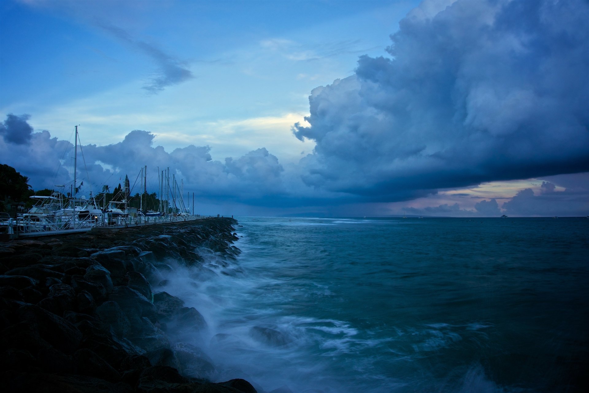 A serene 4K Ultra HD desktop wallpaper showing a blue ocean coastline with boats docked near the coast under a dramatic cloudy sky at the horizon.